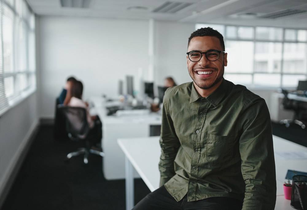 Man at workplace smiling while co-workers talk in the background.