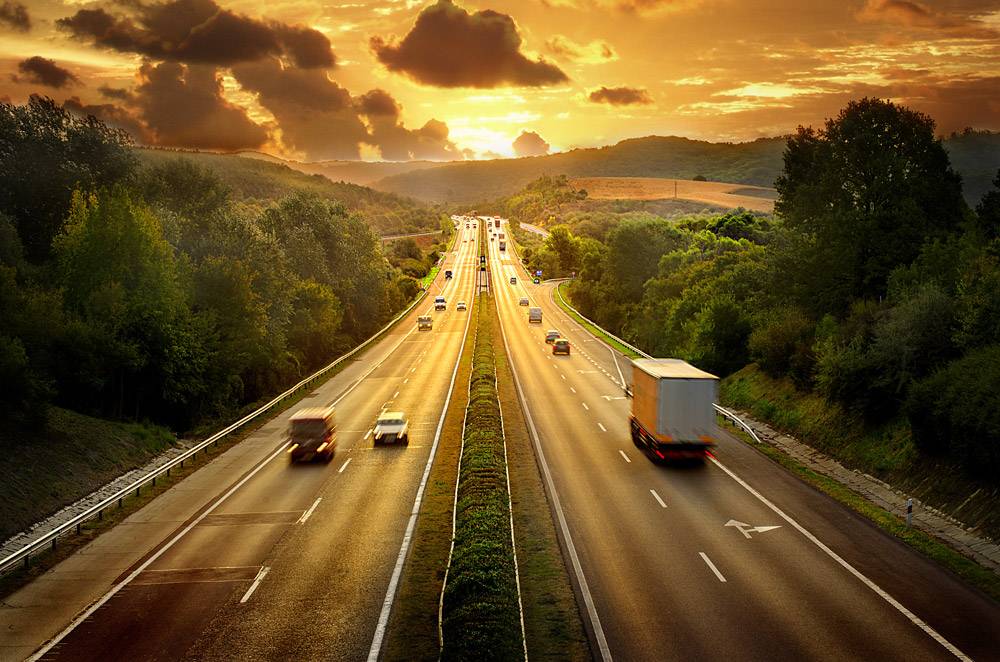 Cars driving on two-sided roadway at sunset. DOT background screening concept.
